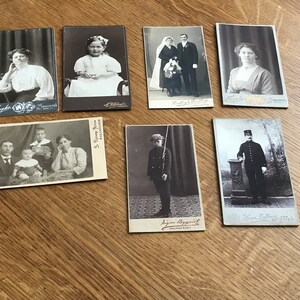 May include: A collection of vintage black and white photographs in various sizes. The photos feature portraits of individuals and families, including a young girl in a dress, a couple, a woman, a family with three children, a young boy in a military uniform, and a man in a military uniform.
