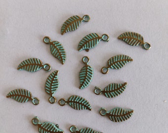 May include: A collection of 14 teal and bronze leaf-shaped charms with a loop at the top. The charms are approximately 1.5 cm long and are arranged on a white surface.