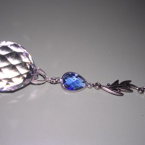 May include: A crystal ball with a faceted surface hangs from a silver chain with two blue gemstone pendants.