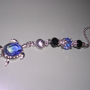 May include: A silver chain with a blue crystal turtle charm and black and blue beads. The chain is attached to a ceiling fan pull.