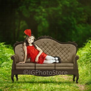 May include: A young person wearing a red dress and a feather headband sits on a brown velvet couch in a green forest setting.