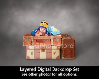 May include: A baby wearing a yellow and blue minion hat is lying on top of two vintage suitcases. A blue toy car is next to the baby. The suitcases are on a gray background.