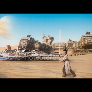 Puede incluir: Un niño con un disfraz de Jedi sostiene un sable de luz brillante en un paisaje desértico. Una nave espacial futurista y estructuras deterioradas se ven al fondo. La escena evoca un tema de ciencia ficción centrado en la aventura y la fantasía.