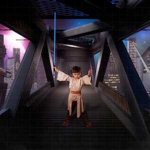 May include: A young person dressed in a light brown robe holds a blue lightsaber in a futuristic setting. The person is standing on a metal walkway with a spaceship flying in the background.