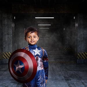 May include: A young boy dressed as Captain America stands in a dark, industrial hallway. He is holding a red, white, and blue shield in his left hand. The hallway is marked with yellow and black warning stripes. The text "Sector 404" is visible on the wall.