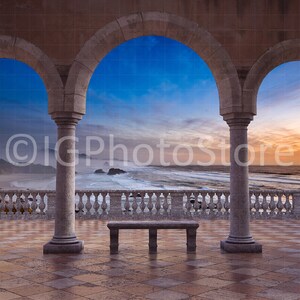 May include: A stone archway with three openings overlooking a beach scene. The sky is a vibrant blue and orange, with clouds in the distance. A wooden bench sits in the center of the archway.