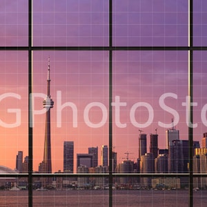 Puede incluir: Una vista del horizonte de Toronto al atardecer, vista a trav&eacute;s de una gran ventana con un patr&oacute;n de cuadr&iacute;cula. La Torre CN es el edificio m&aacute;s alto del horizonte, y otros rascacielos son visibles en la distancia.