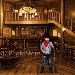 Könnte beinhalten: Ein junger Junge, der als Cowboy verkleidet ist, steht in einem Saloon-Ambiente. Er trägt einen Cowboyhut, ein rotes Bandana, ein kariertes Hemd und Jeans. Er hält ein Spielzeuggewehr in der Hand. Der Saloon hat eine Holztheke, Tische und Stühle. An der Decke hängen Laternen.