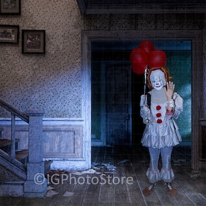 May include: A creepy clown in a white and red costume stands in a dark hallway holding red balloons. The clown is smiling and waving. The hallway has a wooden floor and a staircase in the background.