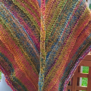 Peut inclure: Un châle tricoté à la main aux couleurs vives, notamment rose, jaune, orange et vert. Le châle présente un motif rayé et un aspect texturé et confortable. L'article est présenté sur un mannequin.