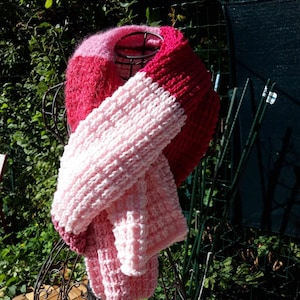 May include: A pink and red knitted scarf with a fluffy texture. The scarf is folded and draped over a black metal stand.