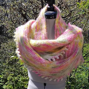 Peut inclure: Un châle tricoté à la main aux couleurs pastel de rose, jaune et vert. Le châle est présenté sur un mannequin, mettant en valeur sa texture douce et ses bords frangés. La laine est un mélange, créant un accessoire chaud et confortable.