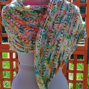 Peut inclure: Un châle tricoté à la main aux couleurs vives, notamment orange, vert et bleu. Le châle est drapé sur un mannequin, mettant en valeur son tricot texturé et son design unique. Le foulard mesure environ 152 cm de long.