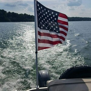 Puede incluir: Un barco en un lago con una bandera de Estados Unidos ondeando en el viento. El barco avanza dejando una estela detrás.