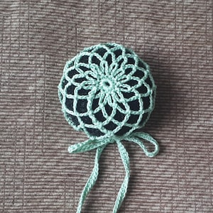 May include: A light green crocheted hair bun cover with a black elastic band and long ties.