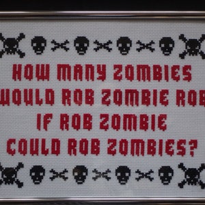 May include: Cross-stitch artwork in a silver frame. The piece features the text "HOW MANY ZOMBIES WOULD ROB ZOMBIE ROB IF ROB ZOMBIE COULD ROB ZOMBIES?" in red, with black skull and crossbones motifs.