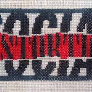 May include: Cross-stitch artwork featuring the words "Social Distancing" in black and red thread on a white background.