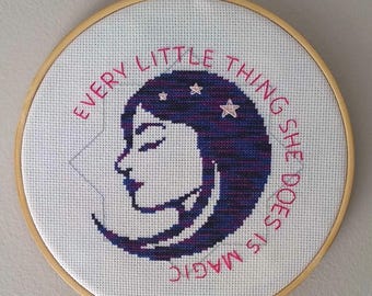 Op de afbeelding: Borduurwerk in een borduurring met een witte achtergrond en een blauw en paars silhouet van een vrouwenhoofd met sterren. De tekst "Every little thing she does is magic" is in roze rond het silhouet geborduurd.