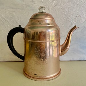 May include: A vintage copper percolator coffee pot with a black handle and a clear glass lid. The pot has a decorative design on the front.