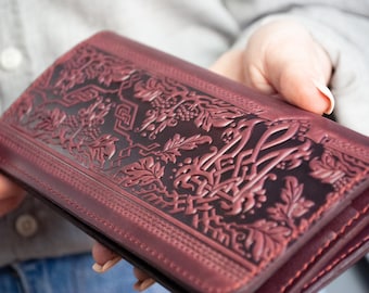 May include: A burgundy leather wallet with an intricate embossed floral design. The wallet is folded and has multiple compartments.