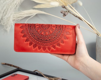 May include: A red leather wallet with a detailed, embossed mandala design. The wallet is rectangular and held in a hand, showcasing its intricate pattern. The wallet's dimensions are approximately 7.5 inches long and 4 inches wide.