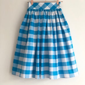 May include: A blue and white gingham midi skirt with a gathered waistband. The skirt is hanging on a wooden hanger.