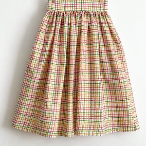 May include: A high-waisted midi skirt with a plaid pattern in shades of cream, green, red, and pink. The skirt has a gathered waistband and a full, flowing silhouette.