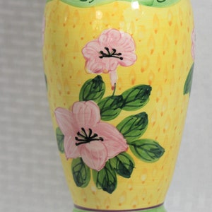 May include: A yellow ceramic vase with a green and blue rim and base. The vase is decorated with pink flowers and green leaves.