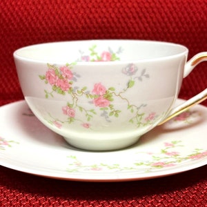 May include: White teacup and saucer set with pink rose floral pattern and gold trim. The cup and saucer feature a delicate design of pink roses and green leaves, perfect for serving tea.