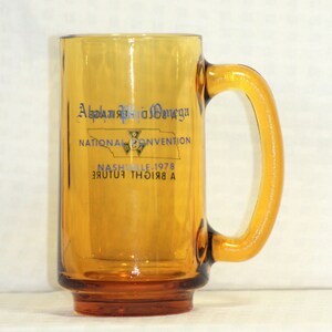 May include: Amber glass mug with a blue and white logo that reads "Alpha Phi Omega National Convention Nashville 1978 A Bright Future".