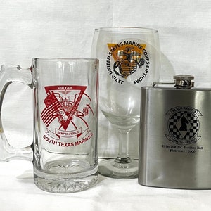 May include: Three glass drinkware items with red and black printed designs. A beer mug with the text "DETAM SOUTH TEXAS MARINES" and a red logo. A wine glass with the text "231st UNITED STATES MARINE CORPS BIRTHDAY". A silver flask with the text "BLACK KNIGHTS HMM-254 (REIN) 231st USMC Birthday Ball November 2006".