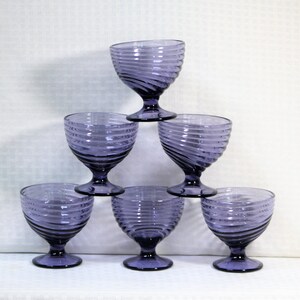Puede incluir: Seis vasos de vidrio morado con un dise&ntilde;o de espiral. Los vasos est&aacute;n apilados en forma de pir&aacute;mide.