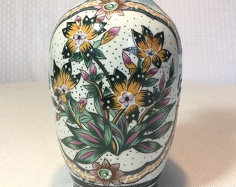 May include: A white ceramic vase with a floral design. The vase has a green rim and base, and the flowers are yellow, pink, and green.