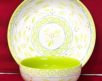 May include: A ceramic bowl and matching plate set featuring a white base with a lime green rim. The design includes a repeating pattern of light green leaves, small yellow and blue dots, and a circular band of stylised green floral motifs.