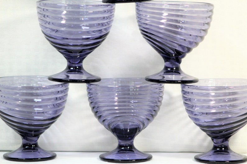 Puede incluir: Conjunto de cinco copas de vidrio morado con un dise&ntilde;o de espiral. Las copas tienen una base de vidrio transparente y un cuenco ancho.