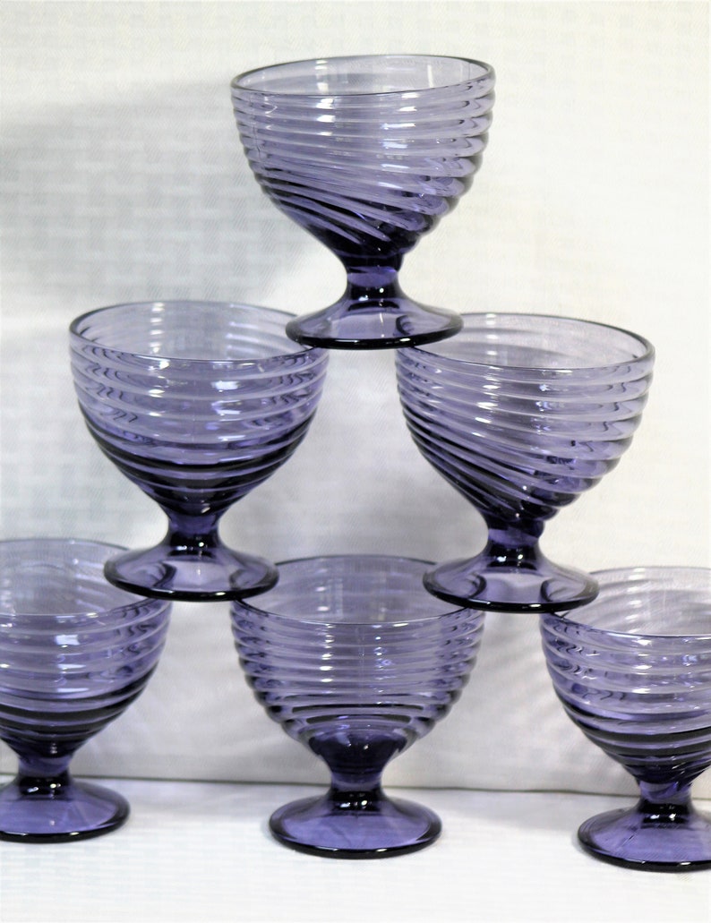 Puede incluir: Seis copas de vidrio morado con un dise&ntilde;o de espiral. Las copas est&aacute;n apiladas en forma de pir&aacute;mide.