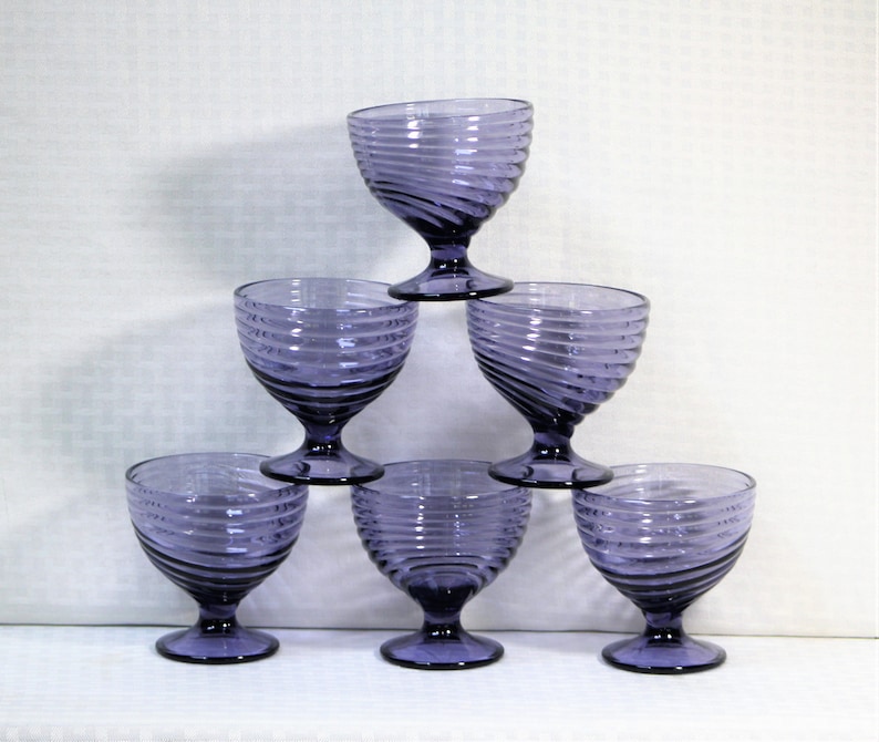 Puede incluir: Seis vasos de vidrio morado con un dise&ntilde;o de espiral. Los vasos est&aacute;n apilados en forma de pir&aacute;mide.