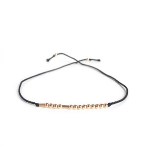 May include: A black string bracelet with gold beads and a gold bar charm.