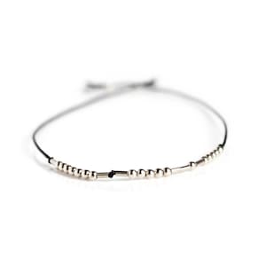 Peut inclure: Un bracelet simple en argent perlé avec un cordon noir. Le bracelet est composé de petites perles rondes et de quelques perles rectangulaires plus longues.
