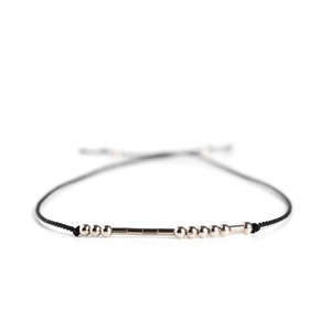 May include: A black string bracelet with silver beads and a silver bar charm.