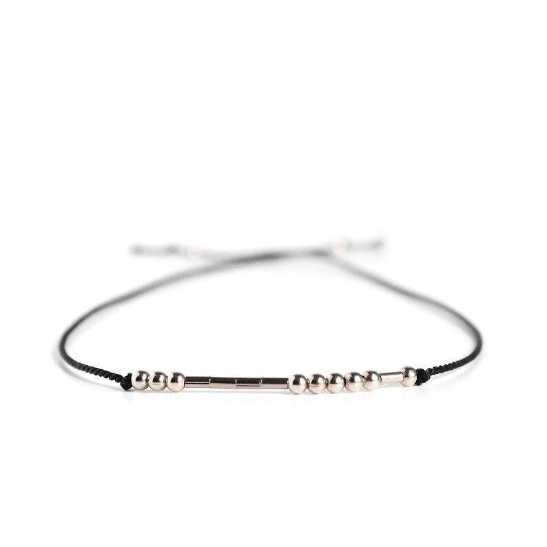 May include: A black string bracelet with silver beads and a silver bar charm.