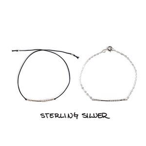 May include: Two bracelets, one with a black cord and silver beads, and the other with a silver chain and silver beads. Both bracelets have a silver bar charm. The text "STERLING SILVER" is written below the bracelets.