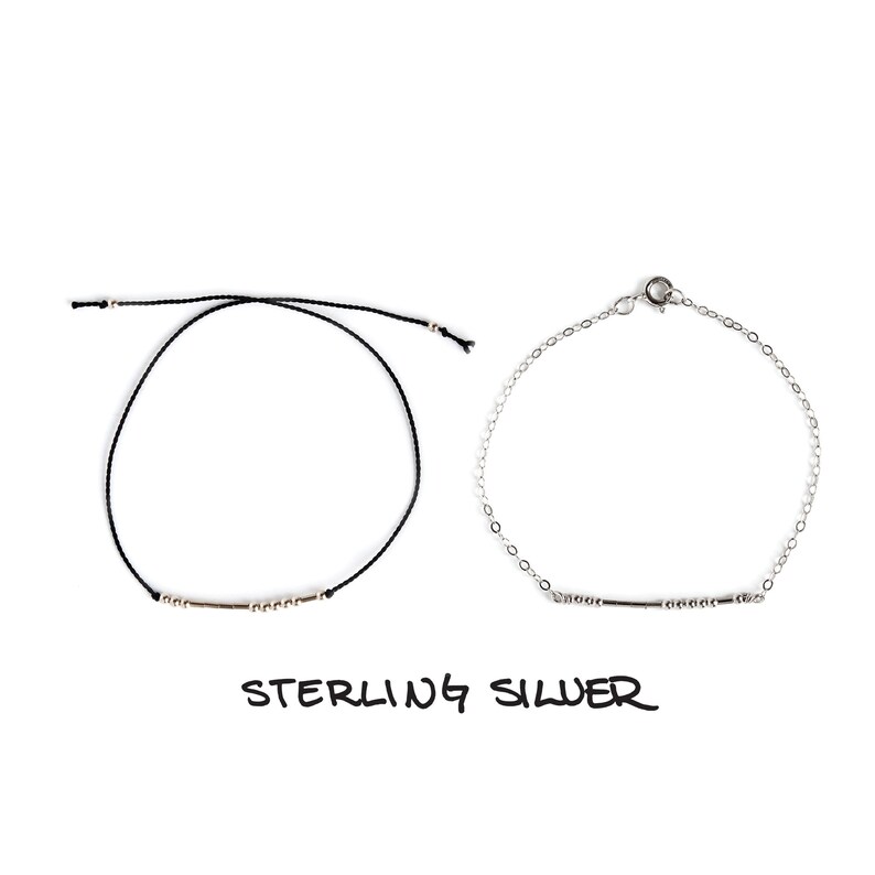 May include: Two bracelets, one with a black cord and silver beads, and the other with a silver chain and silver beads. Both bracelets have a silver bar charm. The text "STERLING SILVER" is written below the bracelets.