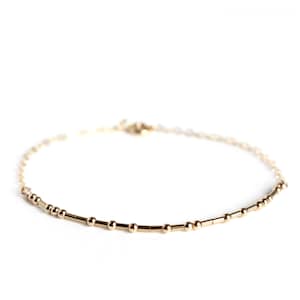 May include: A delicate gold chain bracelet with small round beads and connecting bars.