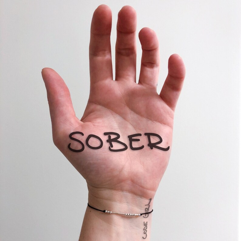 May include: A person's hand with the word "SOBER" written on the palm. The person is wearing a bracelet with the words "CODE GIRL" on it.