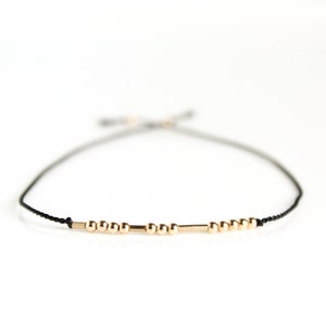 Peut inclure: Un bracelet délicat en cordon noir avec des perles et des accents cylindriques dorés. Le bracelet réglable est conçu avec une fermeture à nœud coulissant. Les perles dorées mesurent environ 0,3 cm de diamètre.