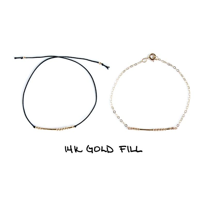 May include: Two bracelets, one with a black cord and one with a gold chain, both with a gold bar and beads. The text "14K GOLD FILL" is written below the bracelets.