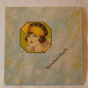 May include: Vintage handkerchief box with a flapper illustration. The box has a light blue background with a yellow and white marbled design. The illustration is of a woman with a yellow headband and a pink collar. The text "Handkerchiefs" is printed on the box.