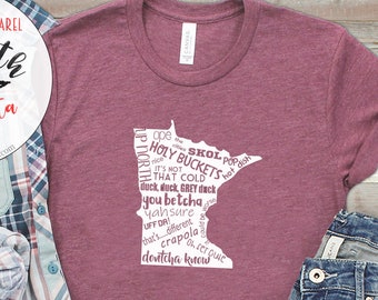 May include: A maroon t-shirt with a white outline of the state of Minnesota filled with text. The text includes "Up North in Minnesota", "Holy Buckets", "You Betcha", "Yah Sure", "Crapola", and "Devitchka Knew".