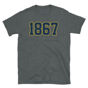 Może przedstawiać: Szary t-shirt z nadrukiem cyfry "1867" w kolorze granatowym z ż&oacute;łtym obramowaniem.
